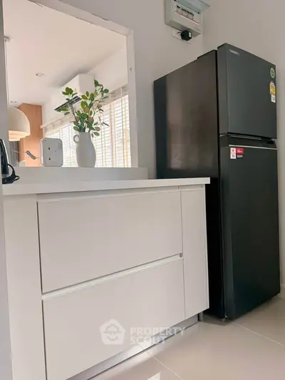 Modern kitchen with sleek black fridge and white cabinetry, featuring an open layout and stylish decor.