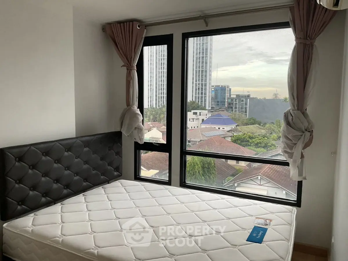 Cozy bedroom with large windows offering a stunning city view, perfect for urban living.