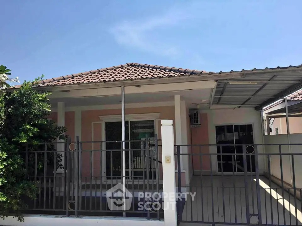 Charming single-story house with tiled roof and gated driveway under clear blue sky.
