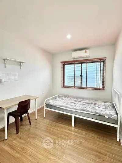 Minimalist bedroom with wooden floor, single bed, desk, and window view.