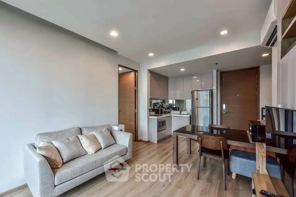 Modern living room with open kitchen, stylish furniture, and wooden flooring.