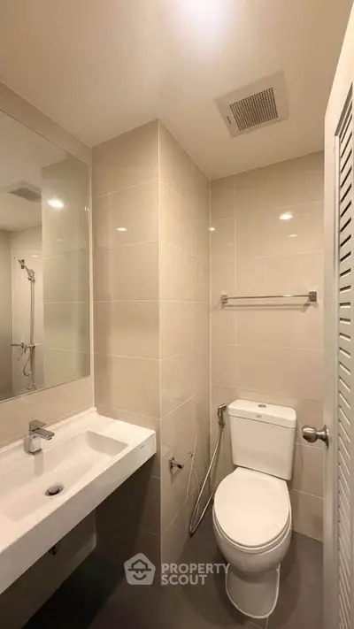 Modern bathroom with sleek fixtures and neutral tiles, featuring a large mirror and efficient layout.