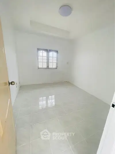 Spacious empty room with tiled flooring and natural light through window.