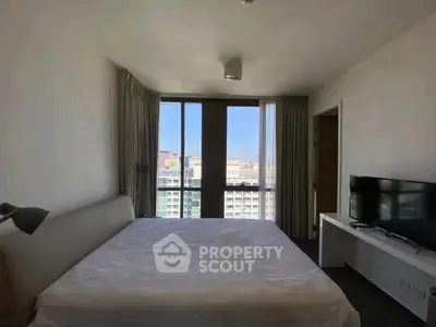 Spacious bedroom with large windows offering city views, modern furnishings, and natural light.