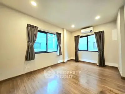 Spacious empty room with wooden flooring and large windows, perfect for customization.