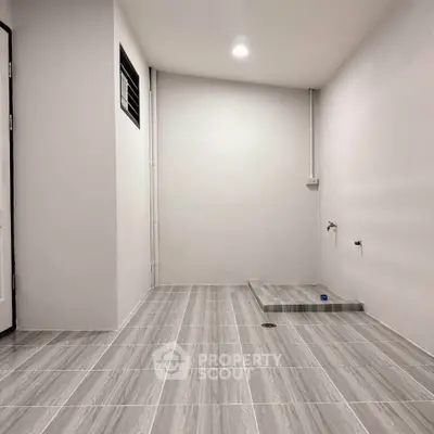 Spacious utility room with tiled flooring and plumbing setup, ideal for laundry or storage.