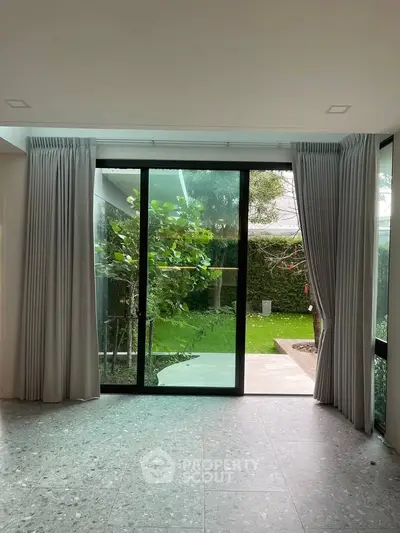 Spacious living room with large glass doors opening to a lush garden view.