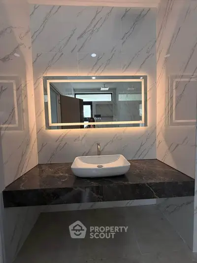 Luxurious bathroom with modern sink and backlit mirror, featuring elegant marble walls.