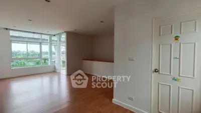 Spacious empty room with wooden flooring and large windows offering natural light and scenic views.