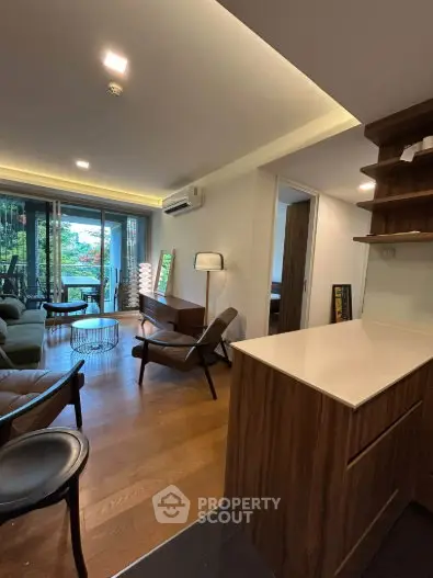 Modern living room with open layout and stylish furniture, featuring a view of greenery through large windows.