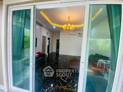 Luxurious living room with marble flooring and elegant chandelier, featuring large glass doors opening to a lush garden view.