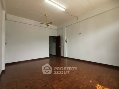 Spacious living room with polished parquet flooring, white walls, and dual ceiling fans, offering a blank canvas for personalized decor.