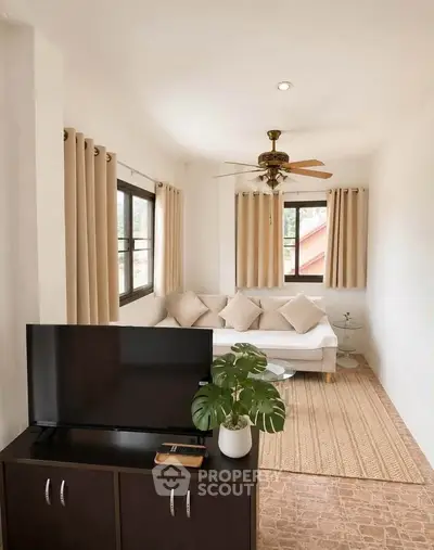 Charming living room with cozy sofa, ceiling fan, and natural light from large windows.