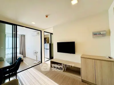 Modern living room with sleek furniture and glass partition leading to bedroom, featuring natural light and minimalist design.
