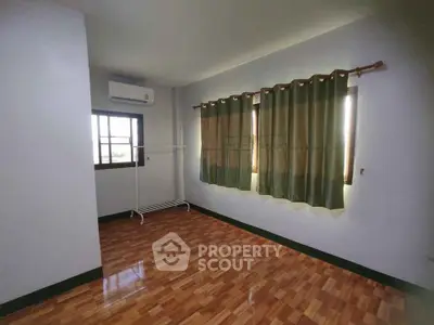 Spacious empty room with wooden flooring and large windows.