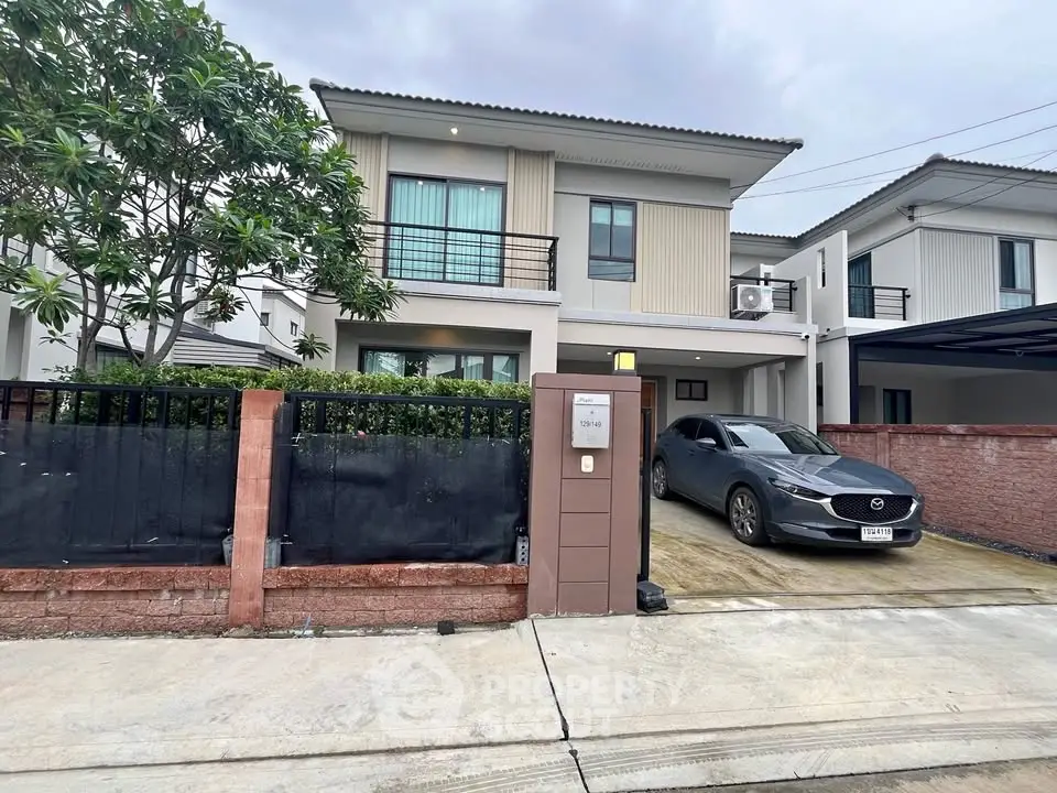 Modern two-story house with driveway and car parked in front, featuring sleek architecture and lush greenery.