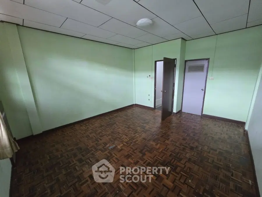 Spacious empty room with parquet flooring and green walls, ideal for customization.