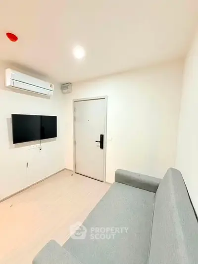 Modern minimalist living room with sleek gray sofa and wall-mounted TV, featuring air conditioning.