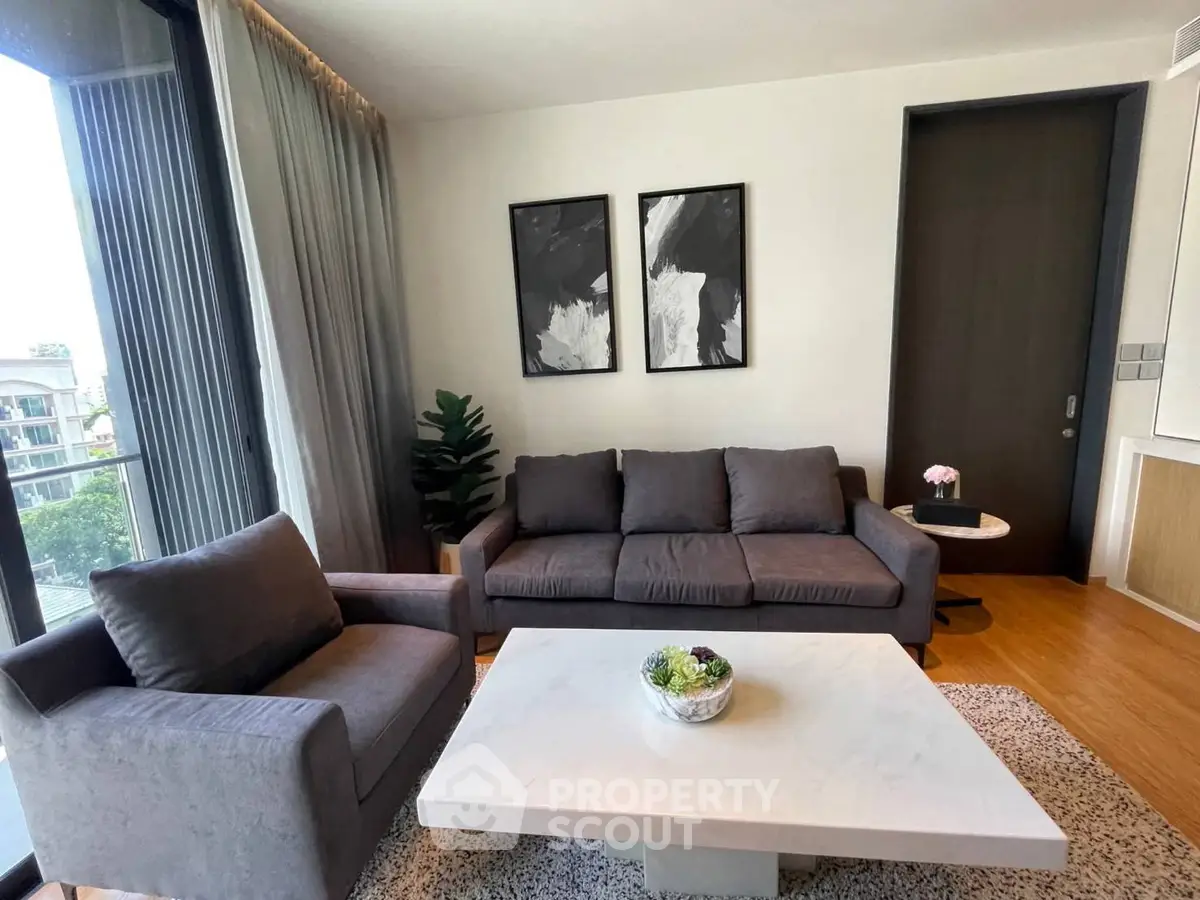 Modern living room with stylish gray furniture and large windows offering natural light and a view.