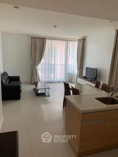 Spacious and bright open-plan living area with gleaming tiled floors, modern kitchen island, and large windows draped in elegant curtains, perfect for entertaining and relaxation.