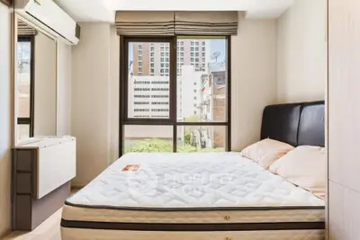 Modern bedroom with large window and city view, featuring a comfortable bed and sleek furnishings.