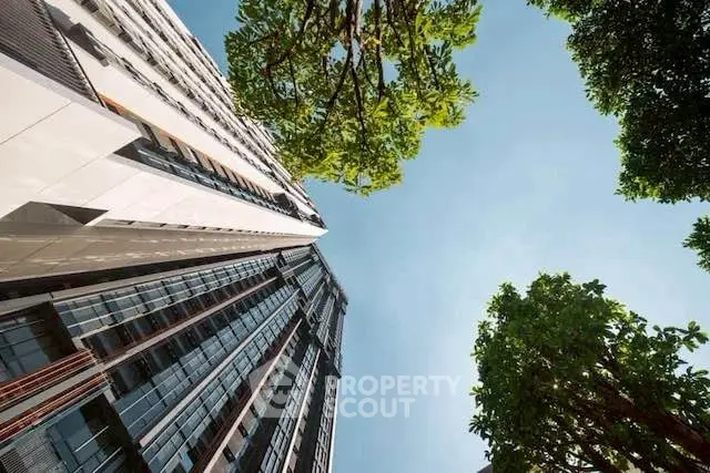 Stunning architectural view of modern high-rise building with lush greenery and clear blue sky.