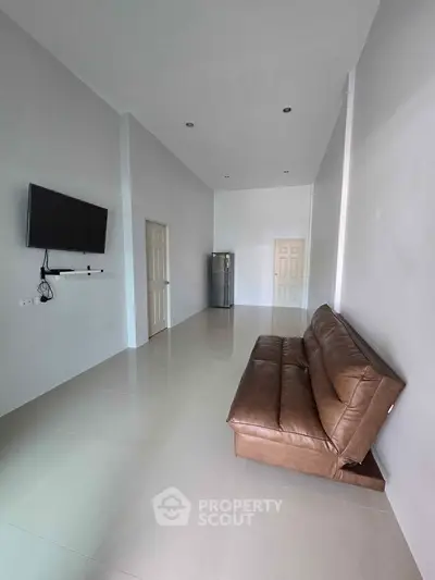 Spacious living room with modern TV and leather sofa, ideal for relaxation.