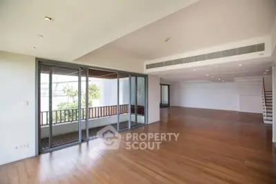 Spacious open-plan living room with wooden flooring and large windows leading to a balcony.