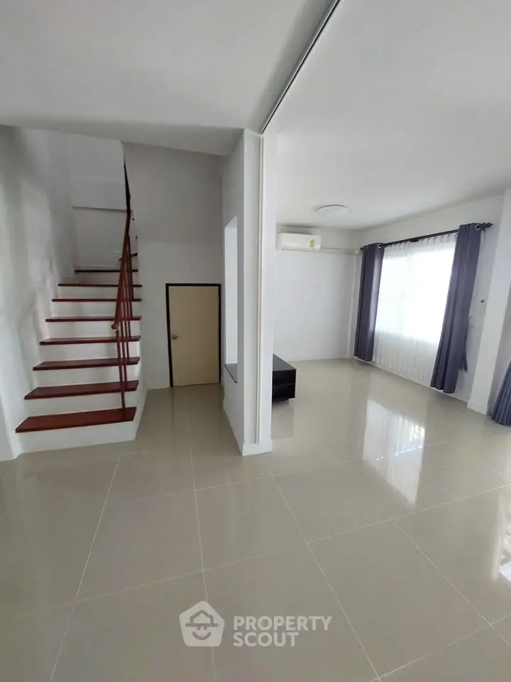 Spacious modern living room with staircase and large windows, perfect for natural light.