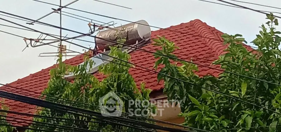 Charming red-tiled roof with solar water heater and lush greenery, perfect for eco-friendly living.