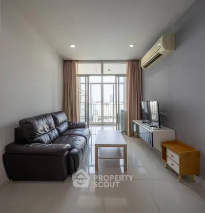 Modern living room with leather sofa, sleek TV unit, and large windows offering city views.