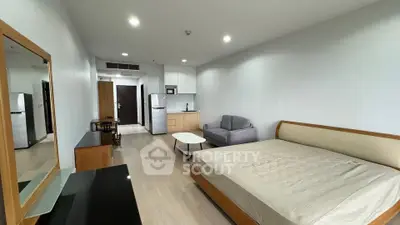 Modern studio apartment with open layout, featuring a cozy bed, sofa, and compact kitchen area.