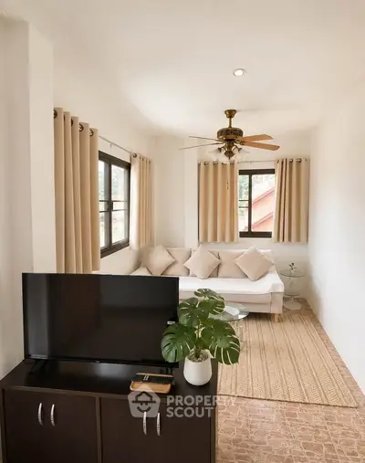 Charming living room with cozy sofa, ceiling fan, and natural light from large windows.