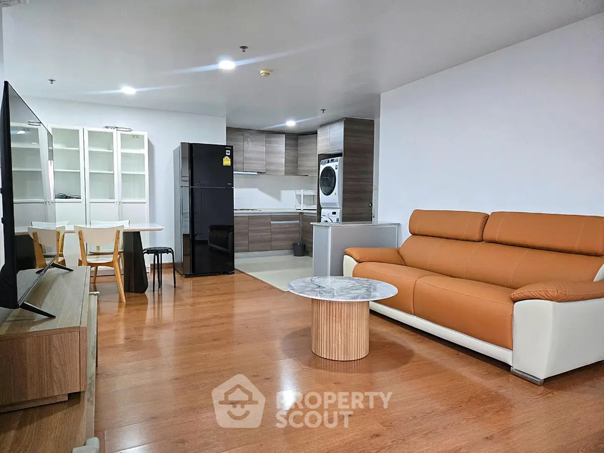 Modern living room with open kitchen, featuring stylish furniture and appliances.