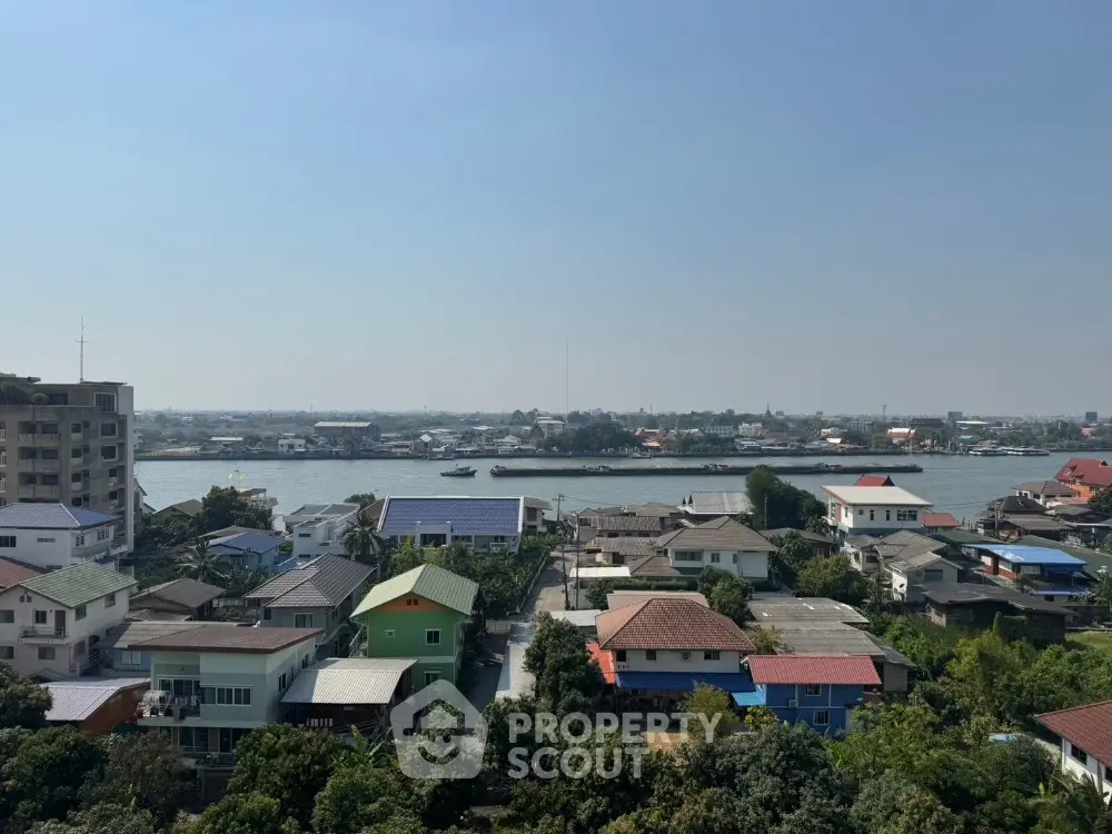 Scenic river view from a residential neighborhood with diverse rooftops and lush greenery.
