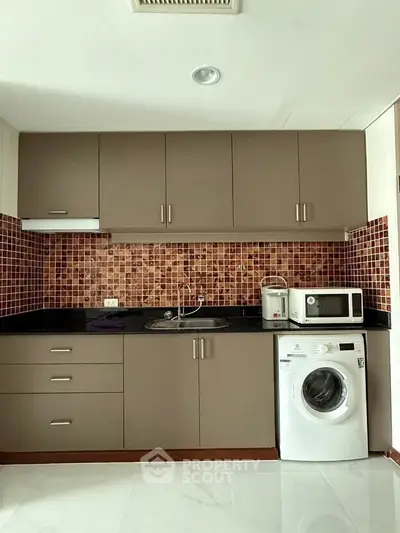 Modern kitchen with brown cabinets, mosaic backsplash, and built-in appliances including washing machine and microwave.