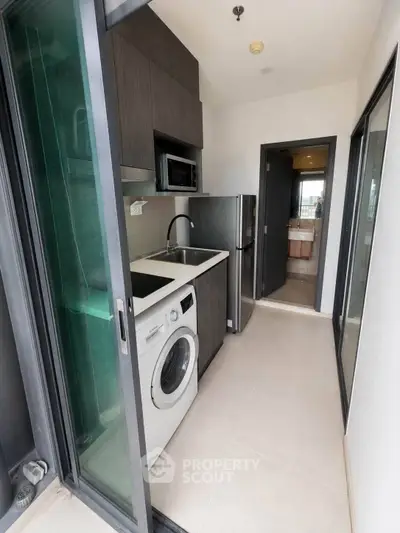 Modern compact kitchen with washing machine and stainless steel appliances in sleek apartment.