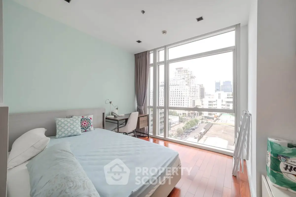 Bright modern bedroom with large windows and city view, featuring stylish decor and wooden flooring.