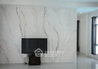 Modern living room with marble accent wall and flat-screen TV, featuring sleek tile flooring and natural light.