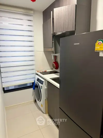 Compact kitchen with modern appliances and washing machine in sleek apartment.