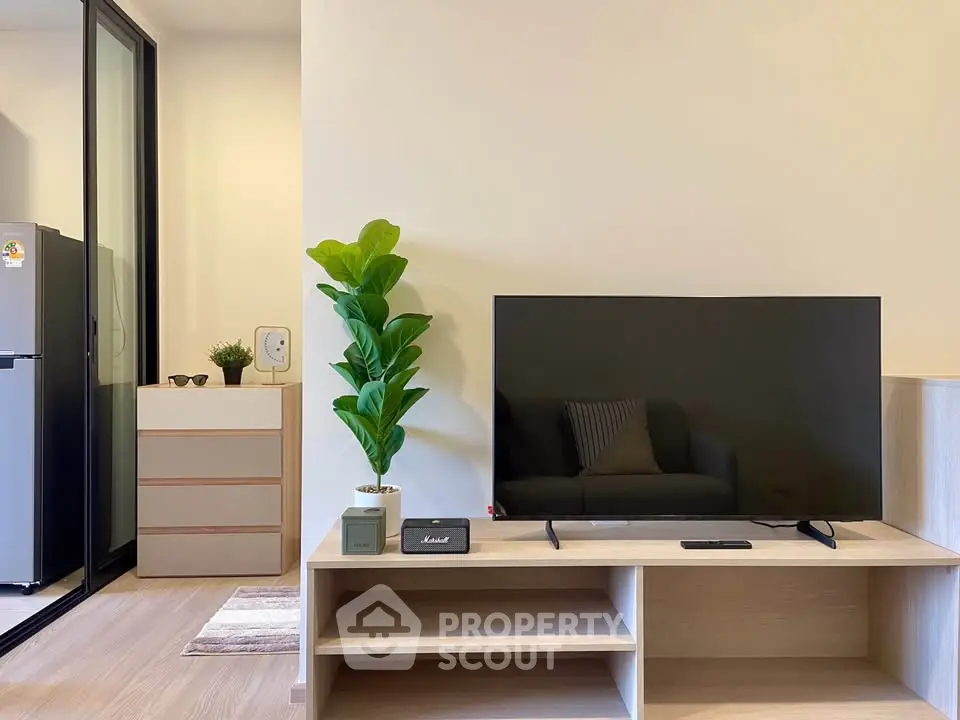 Modern living room with sleek TV stand, potted plant, and sliding glass door to kitchen.
