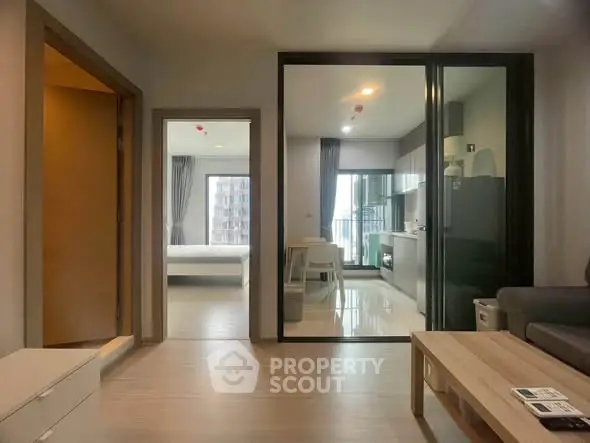 Modern apartment interior with open layout, featuring kitchen and living area, leading to a bright bedroom.