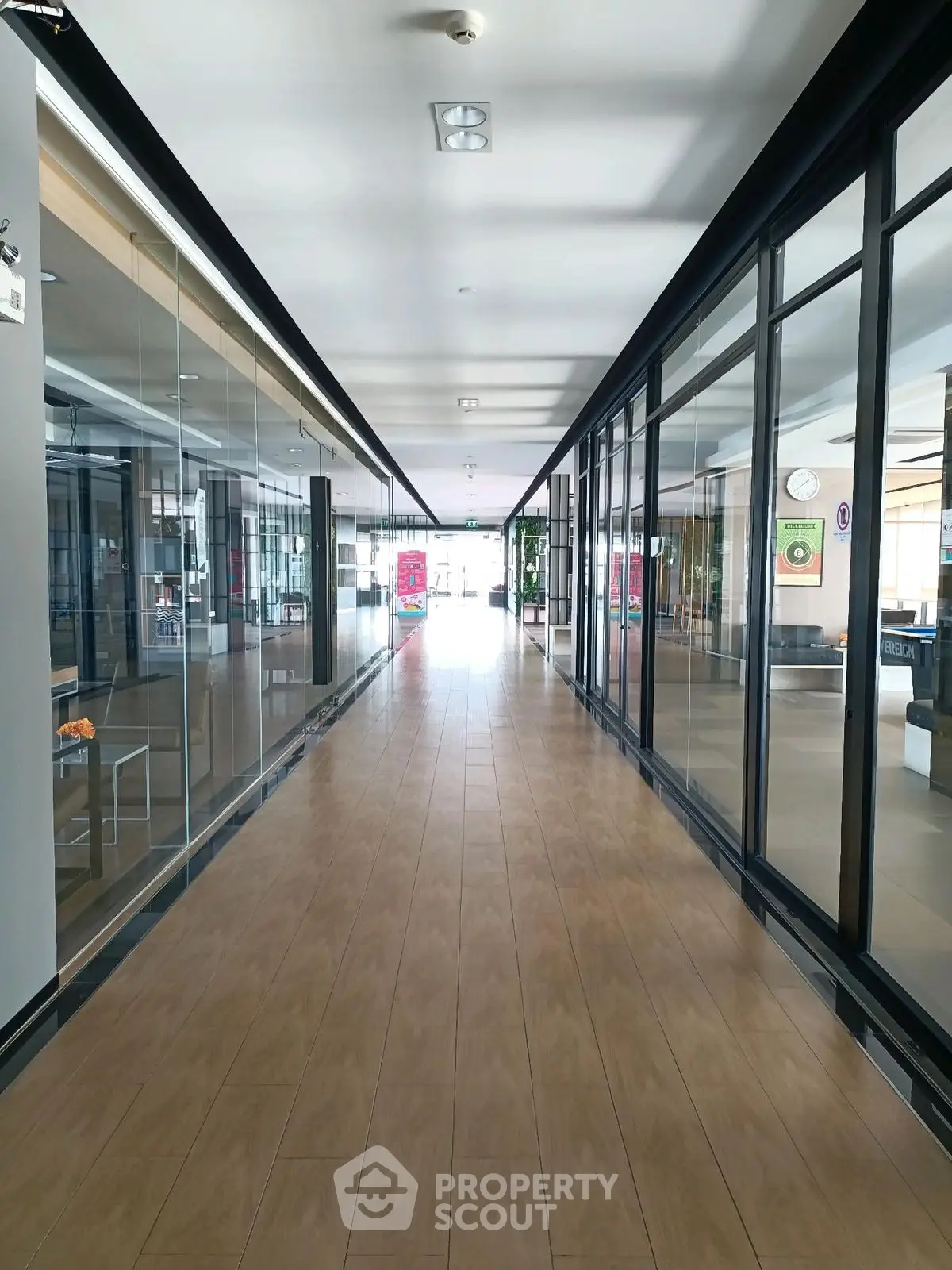 Spacious modern hallway with glass walls and wooden flooring in commercial building.