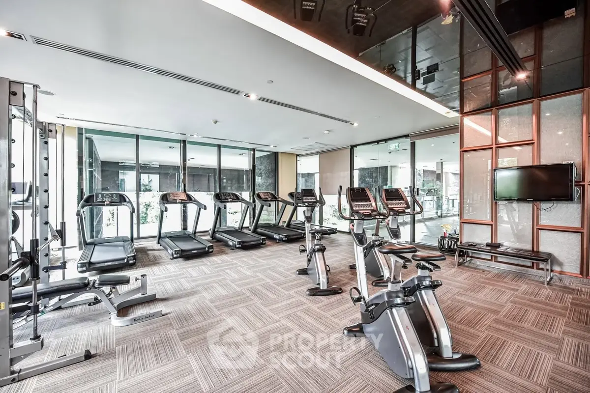 Modern gym with state-of-the-art equipment and floor-to-ceiling windows in luxury residential building.