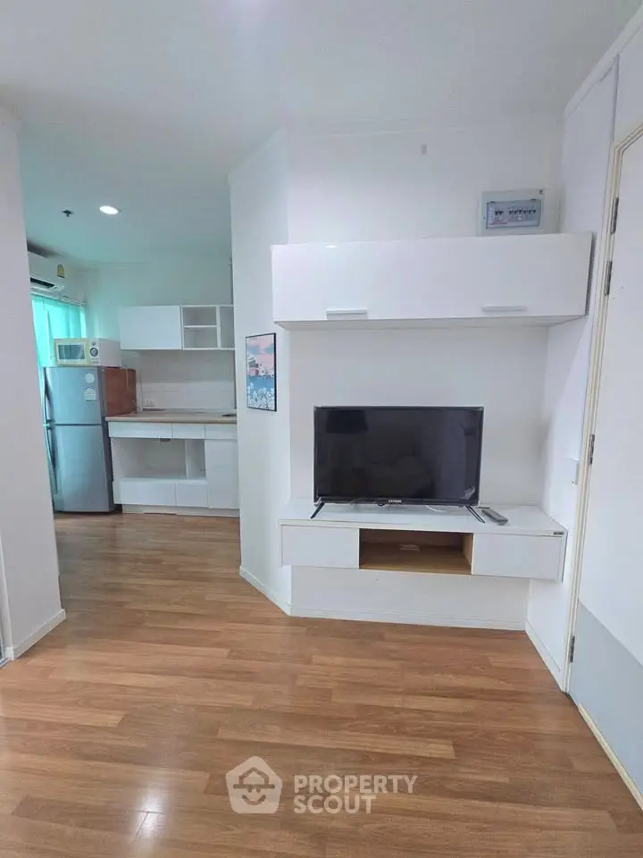 Modern living room with sleek TV unit and open kitchen layout, featuring wooden flooring and contemporary design.