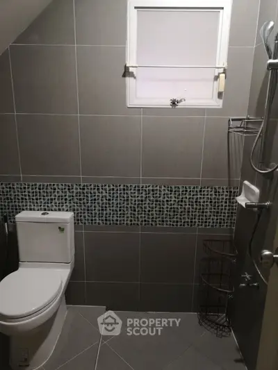 Modern bathroom with sleek gray tiles and mosaic accent, featuring a toilet and shower area.