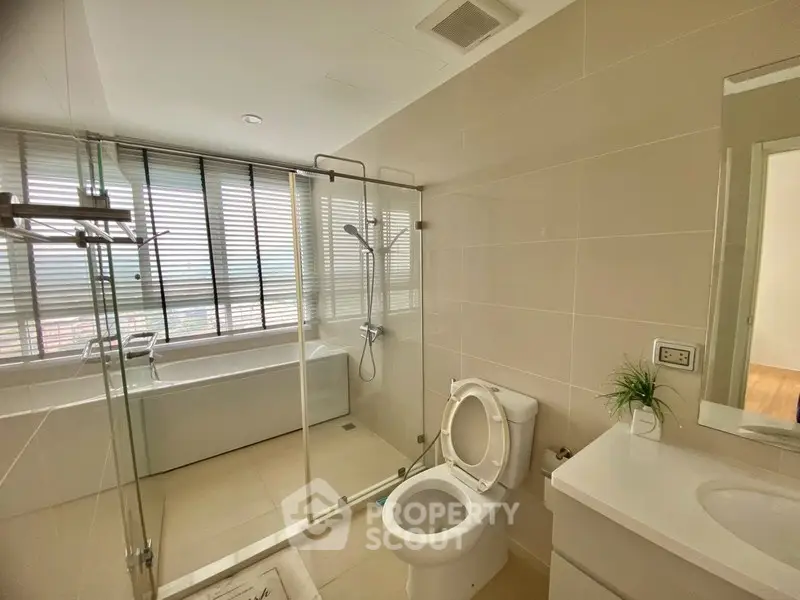 Modern bathroom with glass shower and bathtub in a bright apartment.