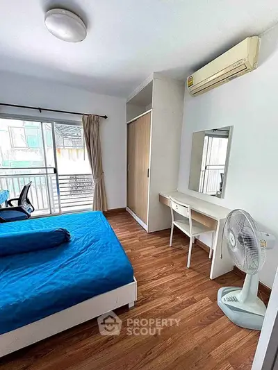 Bright bedroom with balcony access, featuring wooden flooring, air conditioning, and a stylish workspace.