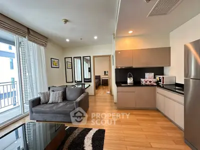 Modern open-layout living room with sleek kitchen and cozy seating area, featuring large windows and stylish decor.