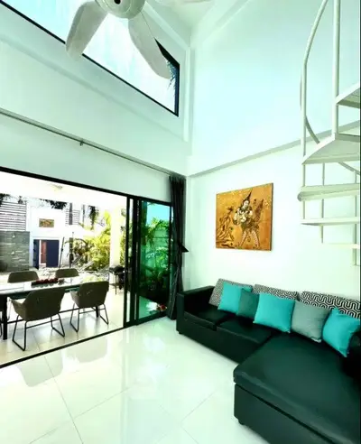 Stunning modern living room with high ceiling and spiral staircase, opening to a lush outdoor patio.